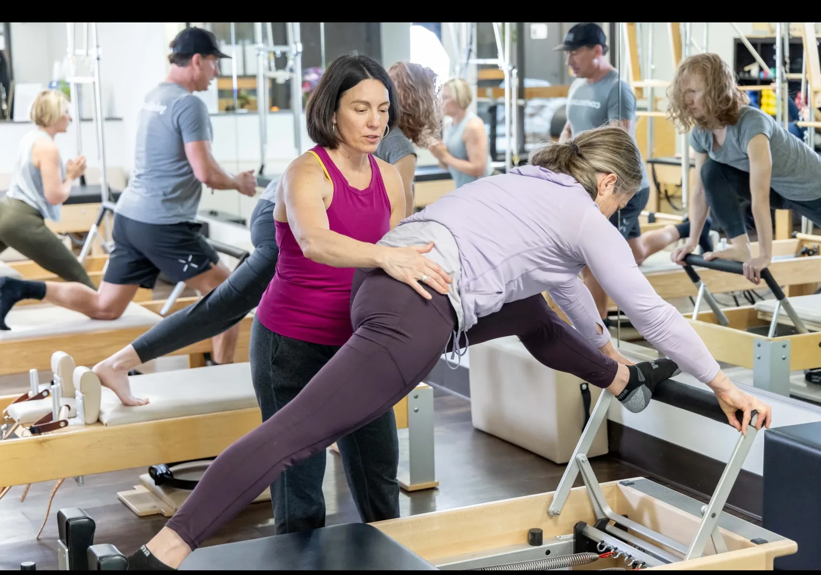 A busy, warm Pilates studio in Boulder with classic wooden reformers and an instructor giving hands-on correction